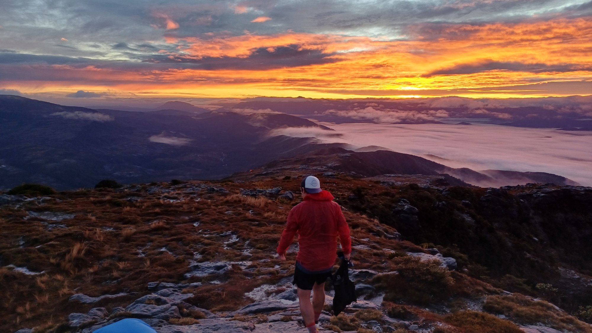 A runner on a rocky ridge at sunrise, with cloud filling the valleys below.